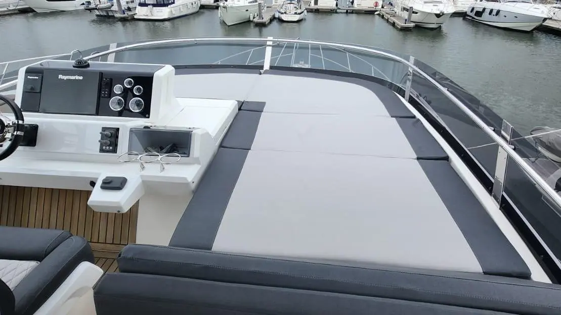 Luxury boat helm with a Raymarine dashboard, seating area, and view of marina moored boats and calm water.